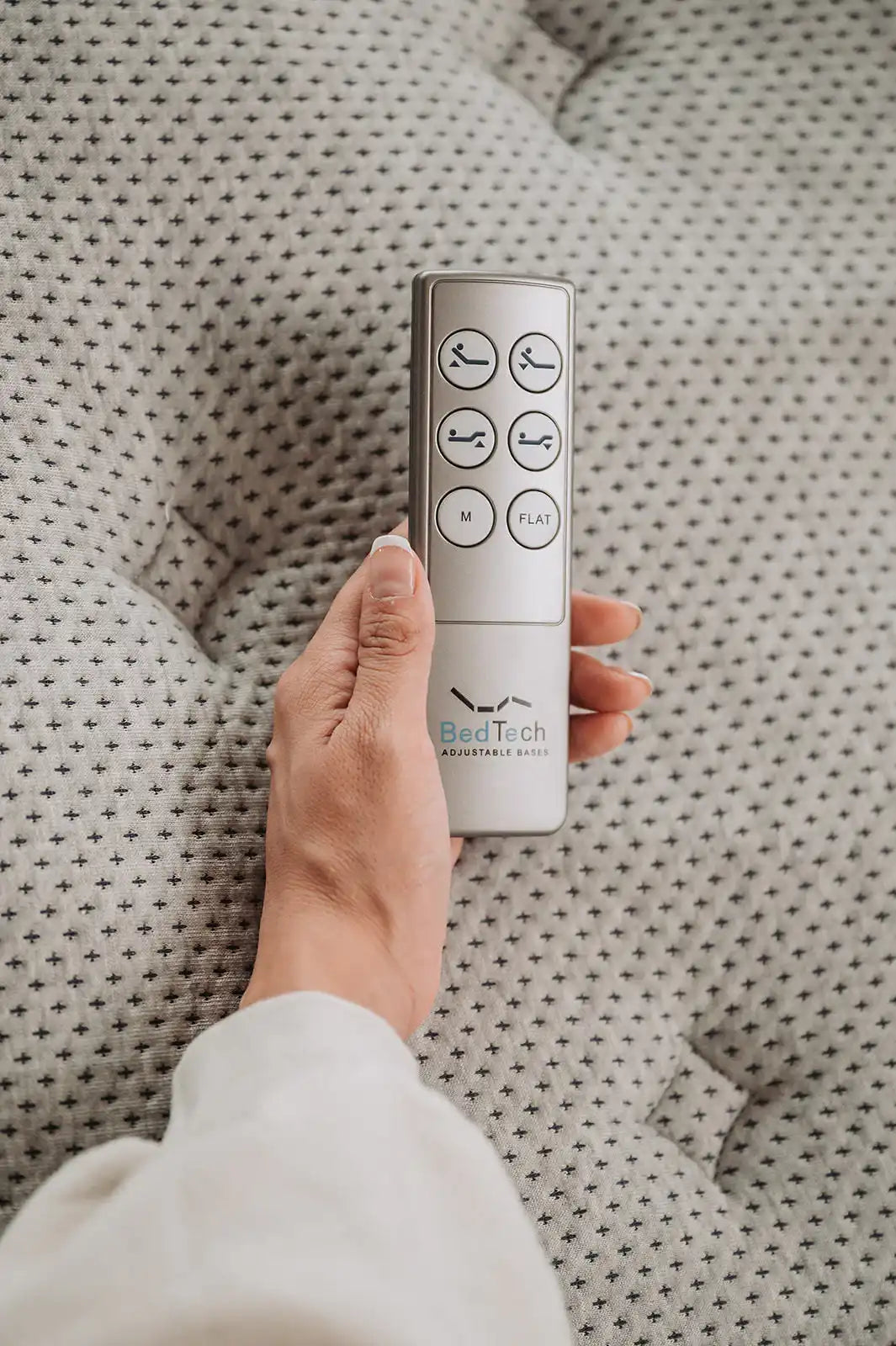 Hand holding BedTech adjustable base remote on patterned mattress