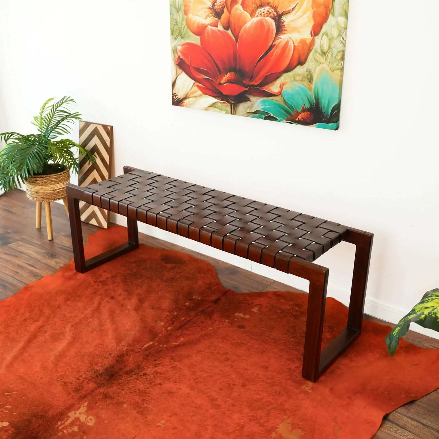 Modern woven leather bench on red cowhide rug, with plant and floral wall art in a living room