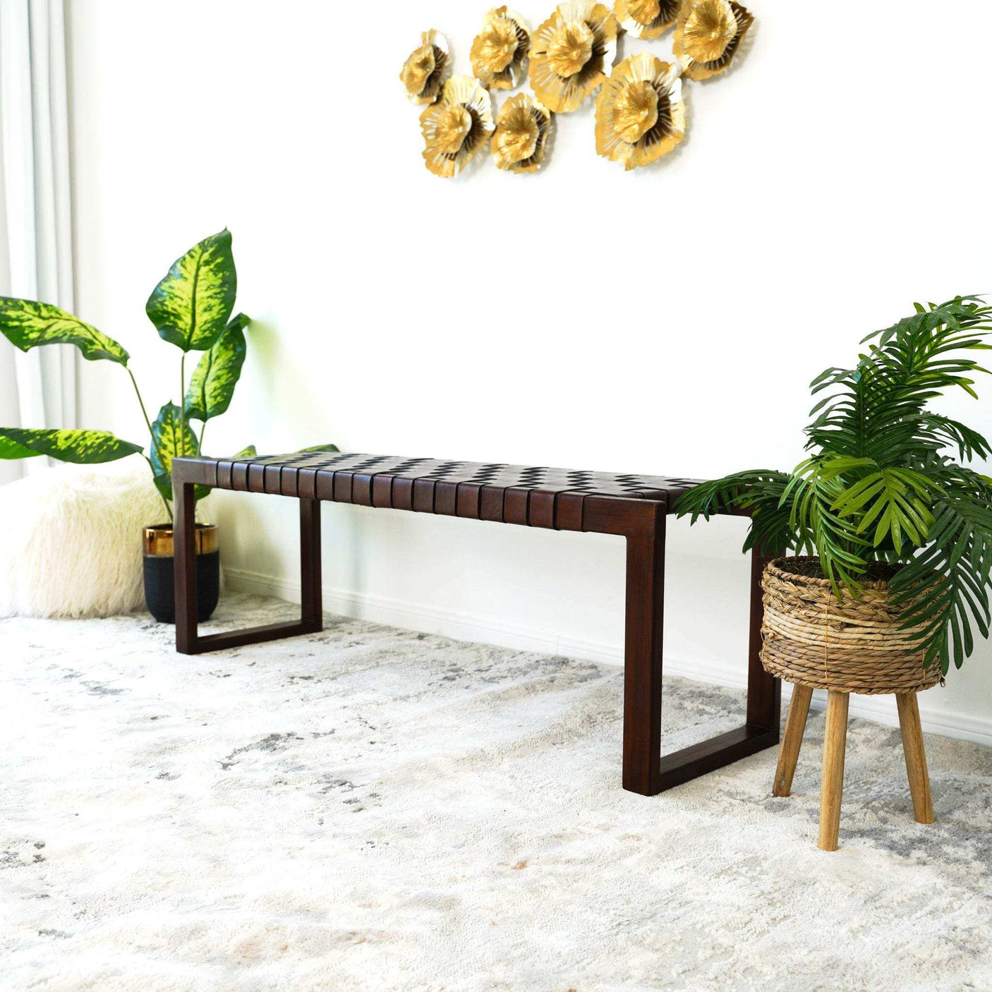 Modern entryway with dark wood bench, woven plant basket, gold wall decor, and large green plants