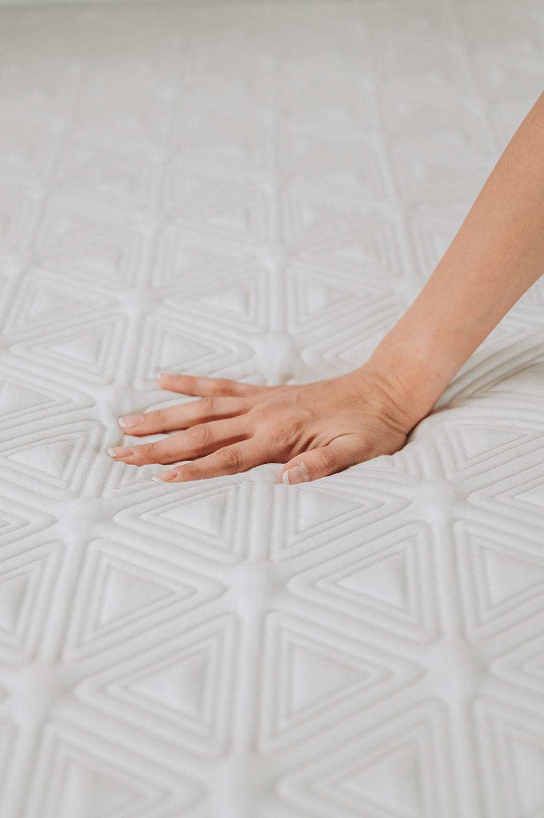 Hand pressing on white memory foam mattress with geometric textured pattern