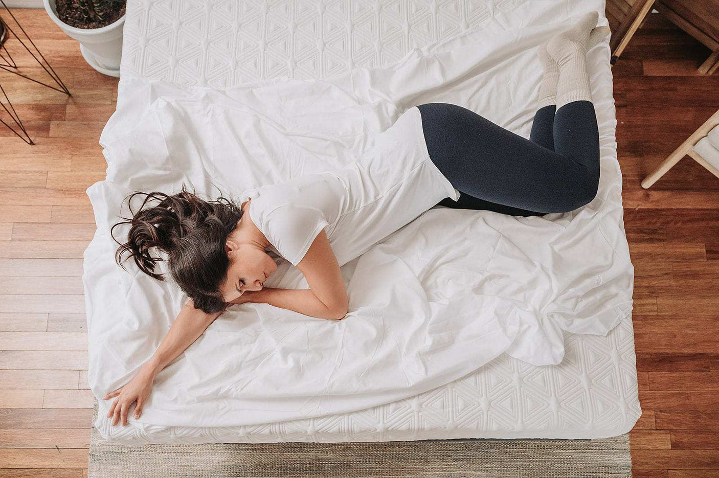 Woman in white shirt and dark leggings sleeping on white bed in cozy bedroom