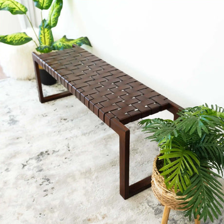 Modern woven wooden bench on a textured rug, surrounded by green potted plants