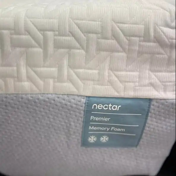 Close-up of a mattress corner showing a white quilted top layer, a textured white side panel, and a blue-gray label that reads 'nectar Premier Memory Foam'.