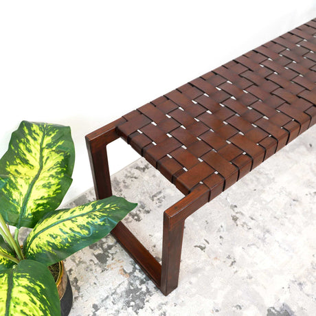 Woven dark wood bench on a light rug beside a potted green plant in a modern room