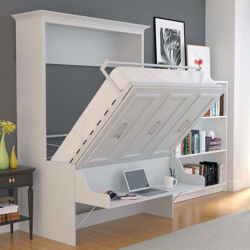 White vertical Murphy bed with desk in modern bedroom, laptop and books on desk, bookshelf nearby.